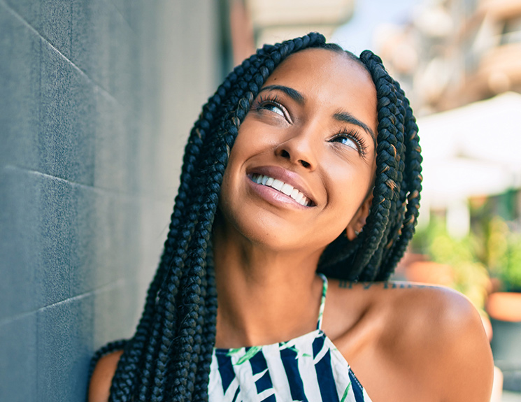 black model with black hair braided smiling and looking up while outdoors