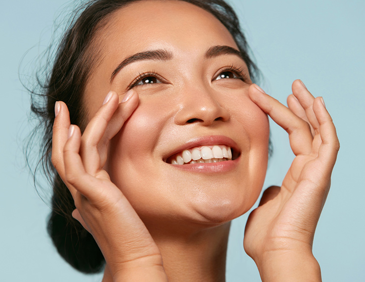 asian model holding the side of her face while smiling